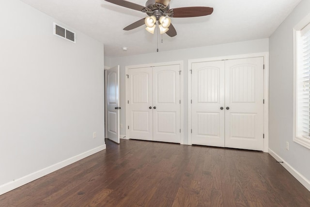 unfurnished bedroom featuring dark wood-style floors, visible vents, baseboards, and two closets