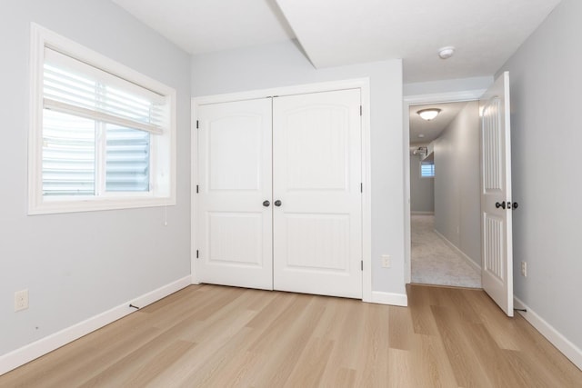 unfurnished bedroom with light wood-style flooring, baseboards, and a closet