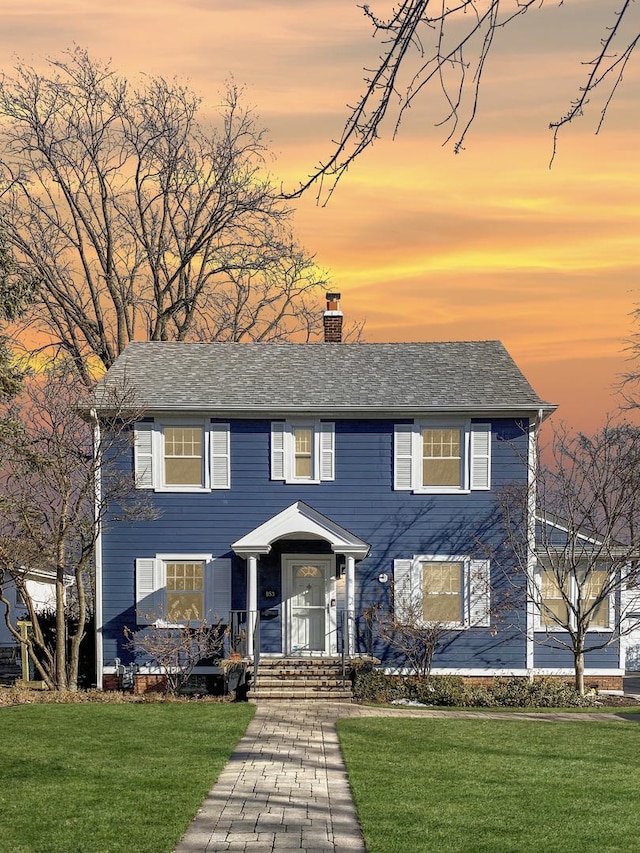 colonial house featuring a chimney and a front yard