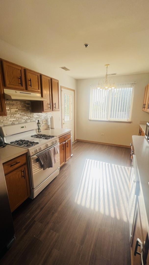 kitchen featuring white gas range oven, hanging light fixtures, fridge, dark hardwood / wood-style floors, and tasteful backsplash