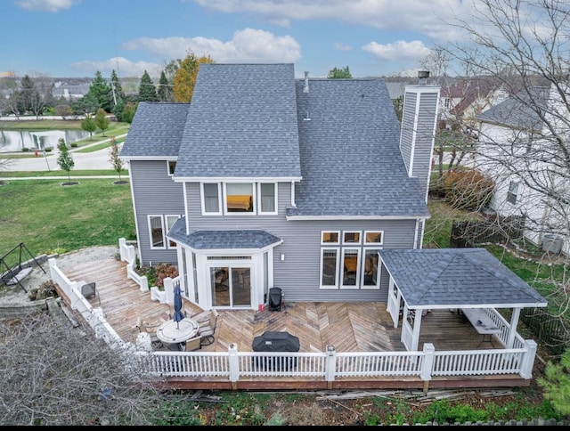 back of house with a chimney, a deck, a lawn, and roof with shingles