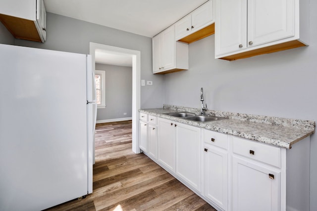 kitchen with freestanding refrigerator, white cabinetry, a sink, and wood finished floors