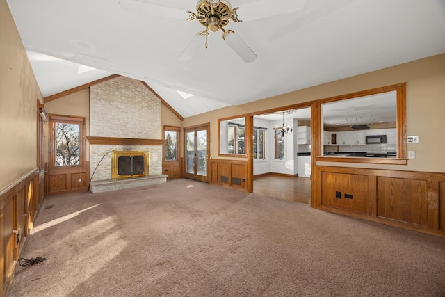 unfurnished living room with lofted ceiling, ceiling fan with notable chandelier, a fireplace, and dark colored carpet