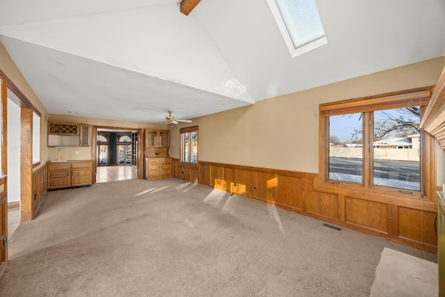 unfurnished living room featuring light carpet, lofted ceiling with skylight, ceiling fan, and wood walls