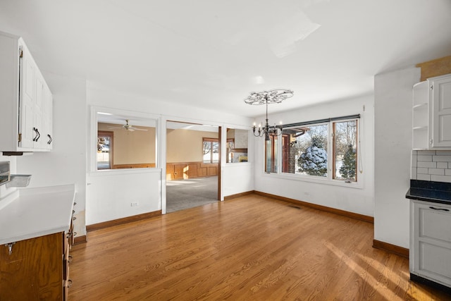 unfurnished dining area with a healthy amount of sunlight, ceiling fan with notable chandelier, and light hardwood / wood-style flooring