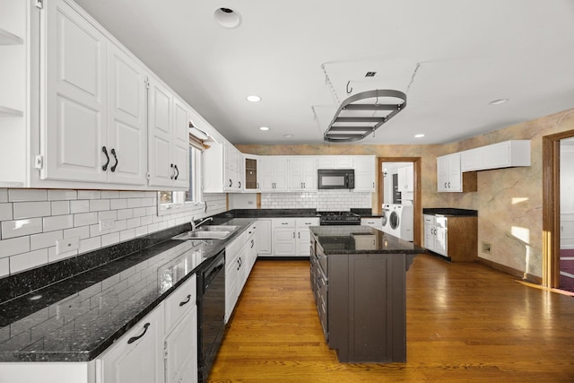 kitchen with sink, black appliances, white cabinets, a kitchen island, and washer / dryer