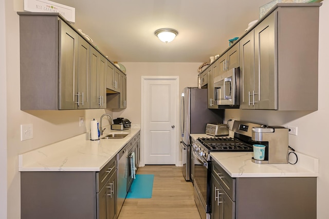 kitchen with sink, gray cabinetry, light wood-type flooring, appliances with stainless steel finishes, and light stone countertops