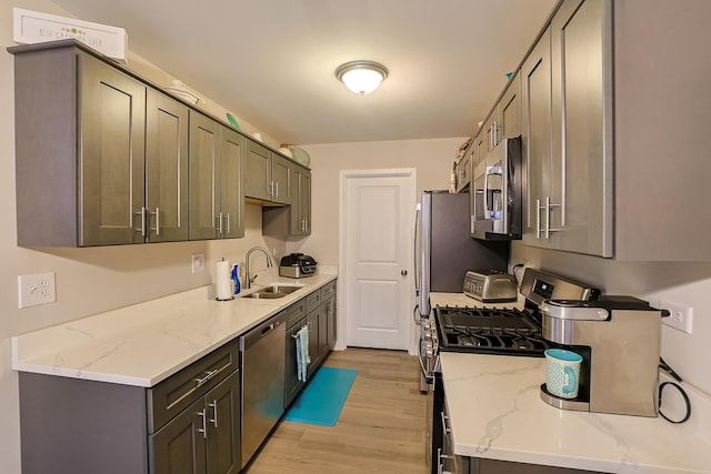 kitchen with light stone countertops, appliances with stainless steel finishes, sink, and light wood-type flooring