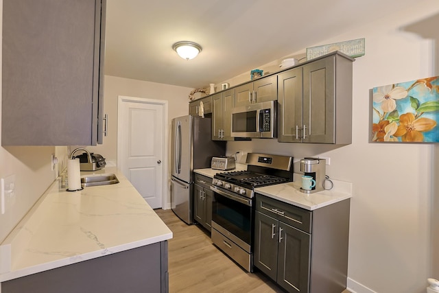 kitchen with sink, gray cabinetry, light hardwood / wood-style flooring, appliances with stainless steel finishes, and light stone countertops