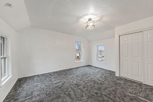 unfurnished bedroom with lofted ceiling, dark carpet, a closet, and a textured ceiling