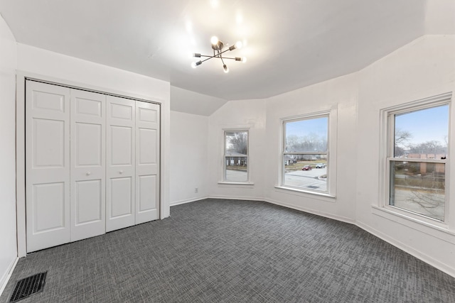 unfurnished bedroom featuring multiple windows, vaulted ceiling, a closet, and dark colored carpet