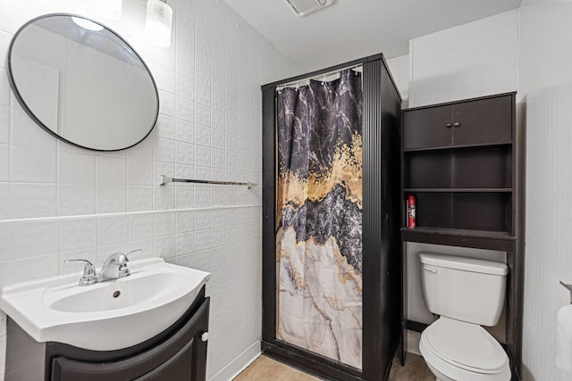 bathroom with walk in shower, vanity, toilet, and tile walls