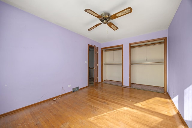 unfurnished bedroom with multiple closets, ceiling fan, and hardwood / wood-style flooring