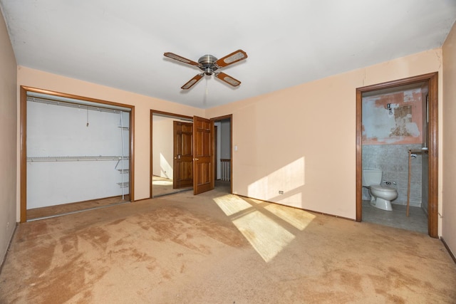 unfurnished bedroom with connected bathroom, two closets, light colored carpet, and ceiling fan