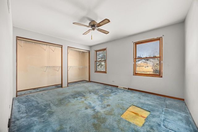 unfurnished bedroom with multiple closets, carpet flooring, and ceiling fan