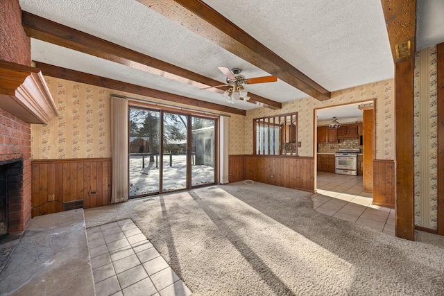 unfurnished living room with wood walls, a brick fireplace, light carpet, a textured ceiling, and beam ceiling