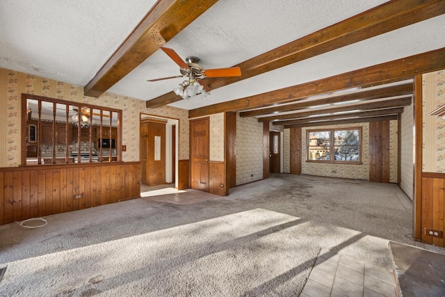 unfurnished living room with ceiling fan, beamed ceiling, a textured ceiling, and carpet flooring