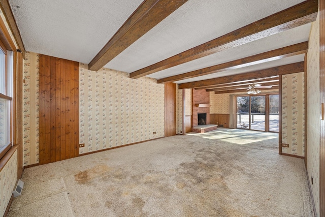 unfurnished living room with beamed ceiling, carpet, a fireplace, and a textured ceiling