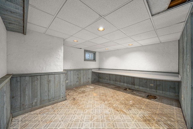 basement featuring a paneled ceiling and wood walls