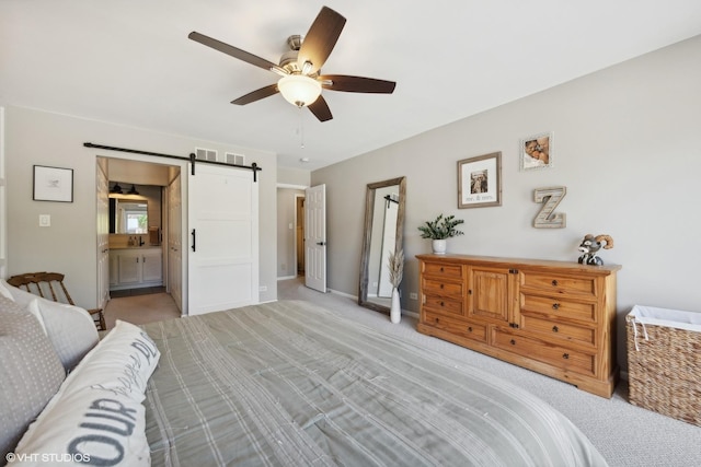 carpeted bedroom with ceiling fan, ensuite bath, and a barn door