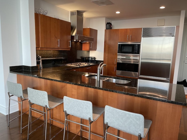 kitchen with a breakfast bar area, built in appliances, range hood, and kitchen peninsula