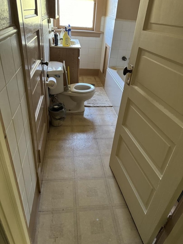 bathroom featuring tile walls, toilet, tile patterned floors, vanity, and a bath