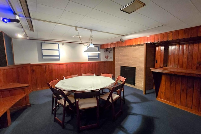 carpeted dining space featuring rail lighting, a brick fireplace, and wood walls