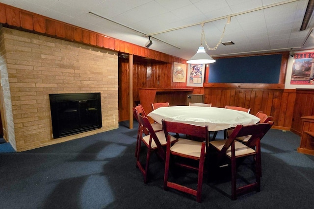 carpeted dining room with wooden walls, a brick fireplace, and rail lighting