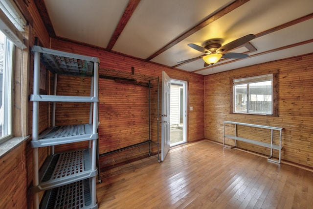 interior space with beam ceiling, ceiling fan, light hardwood / wood-style floors, and wood walls