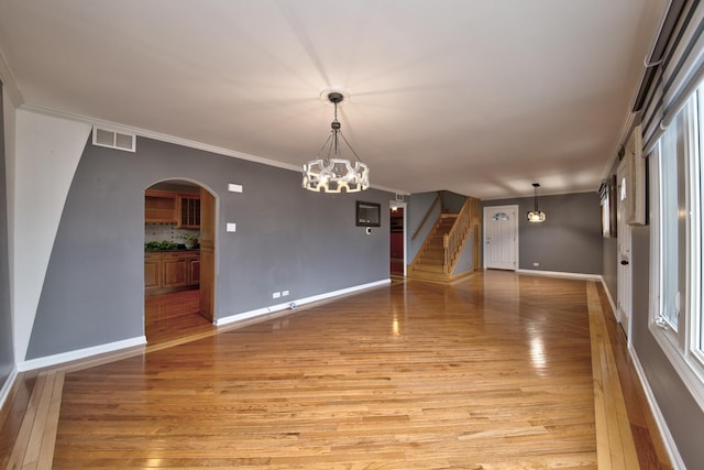 spare room featuring a notable chandelier, ornamental molding, and light wood-type flooring