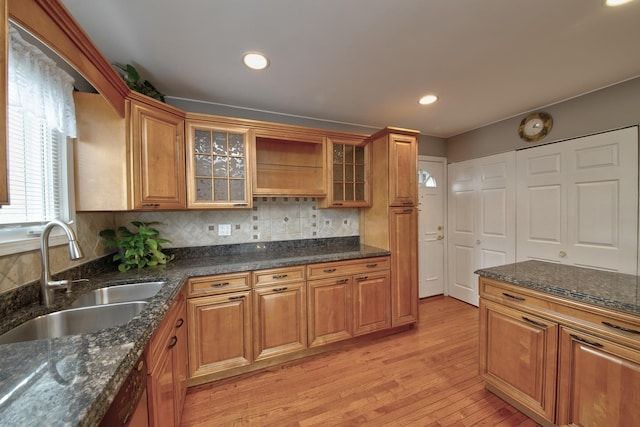 kitchen with sink, light hardwood / wood-style flooring, dishwasher, dark stone countertops, and backsplash