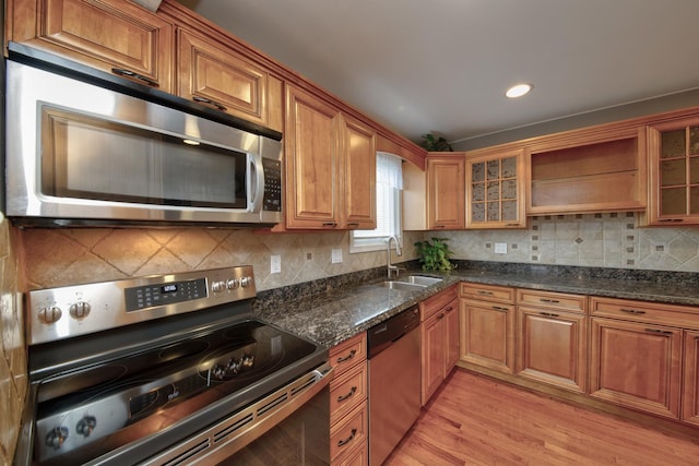 kitchen with tasteful backsplash, sink, dark stone counters, stainless steel appliances, and light wood-type flooring