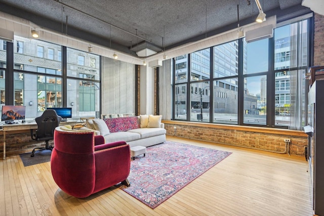 living room featuring wood-type flooring, brick wall, and rail lighting