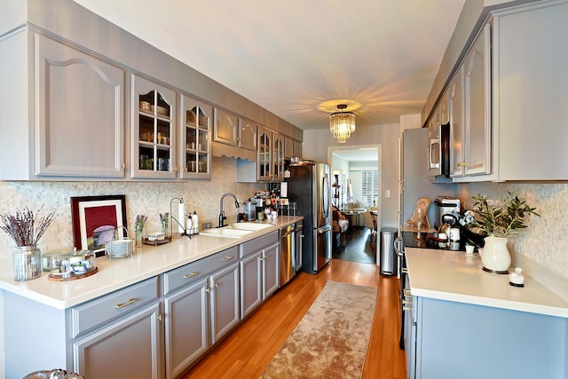 kitchen with appliances with stainless steel finishes, sink, decorative backsplash, hanging light fixtures, and light hardwood / wood-style flooring