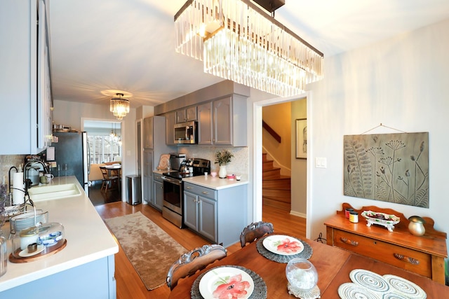 kitchen featuring sink, decorative backsplash, a notable chandelier, stainless steel appliances, and light wood-type flooring