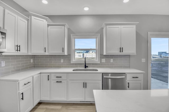 kitchen featuring sink, white cabinets, decorative backsplash, stainless steel dishwasher, and light hardwood / wood-style floors