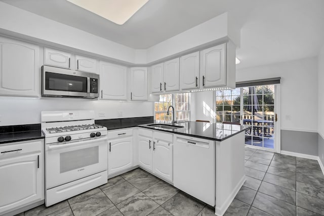 kitchen featuring a sink, dark countertops, white cabinetry, white appliances, and a peninsula