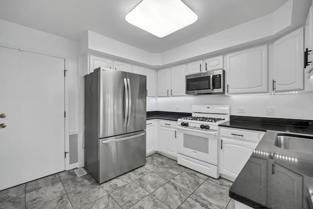 kitchen with white cabinetry, dark countertops, a sink, and stainless steel appliances