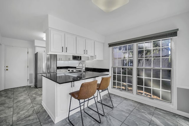 kitchen with freestanding refrigerator, a sink, white cabinetry, dark countertops, and marble finish floor