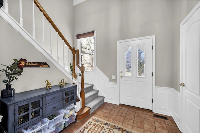 tiled entryway featuring a wainscoted wall, stairway, a decorative wall, and visible vents