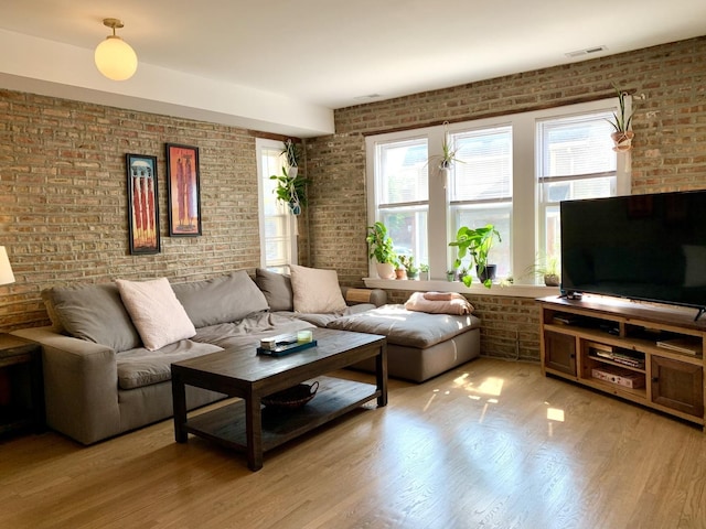 living room with light wood-type flooring, plenty of natural light, and brick wall