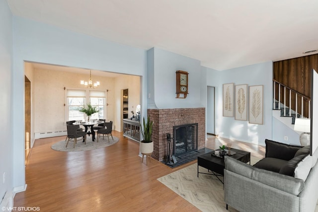 living room with a baseboard radiator, wood finished floors, stairs, a brick fireplace, and an inviting chandelier