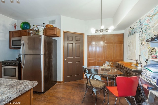 kitchen featuring visible vents, appliances with stainless steel finishes, brown cabinetry, dark wood finished floors, and an inviting chandelier