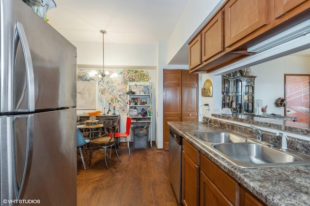 kitchen with brown cabinetry, dark countertops, dark wood-style flooring, stainless steel appliances, and a sink