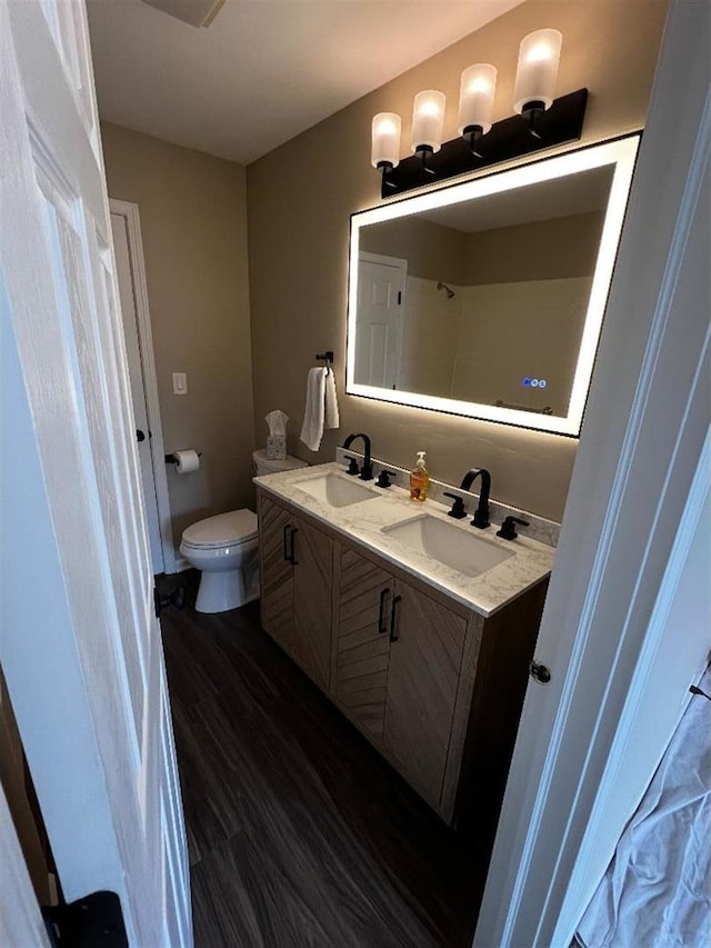 full bathroom featuring double vanity, wood finished floors, a sink, and toilet