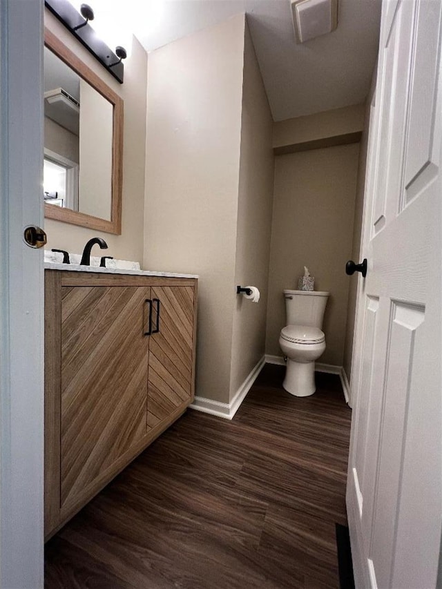 half bathroom with toilet, baseboards, wood finished floors, and vanity