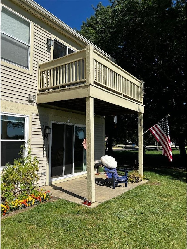 rear view of property with a balcony, a patio area, and a lawn