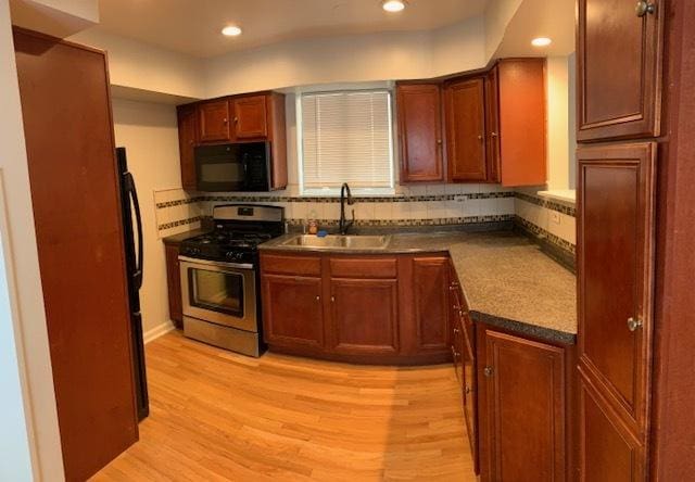 kitchen with stainless steel range with gas cooktop, sink, backsplash, and light hardwood / wood-style floors