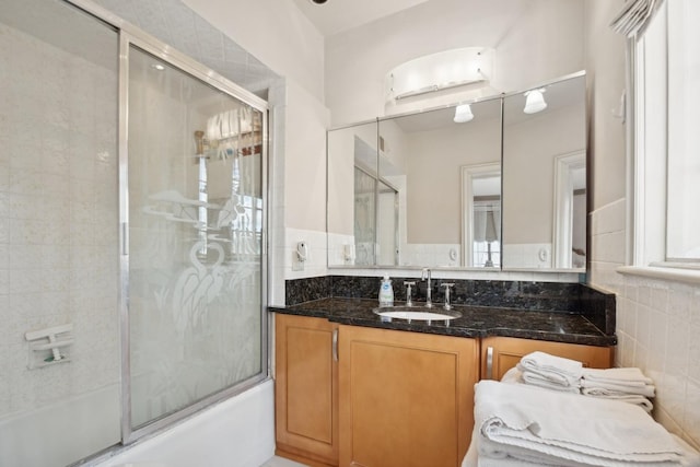 bathroom with tile walls, vanity, and shower / bath combination with glass door