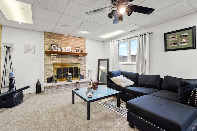 carpeted living room with a drop ceiling, a brick fireplace, and ceiling fan